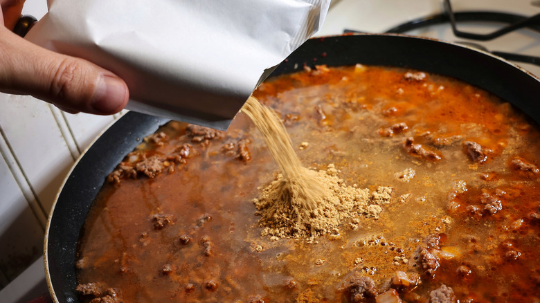 Hand pouring seasoning packet into skillet of Hamburger Helper
