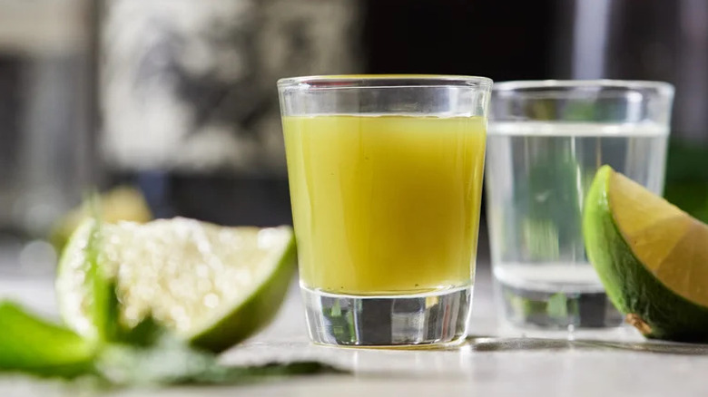 Green chile-infused tequila chaser in shot glass, next to lime wedges