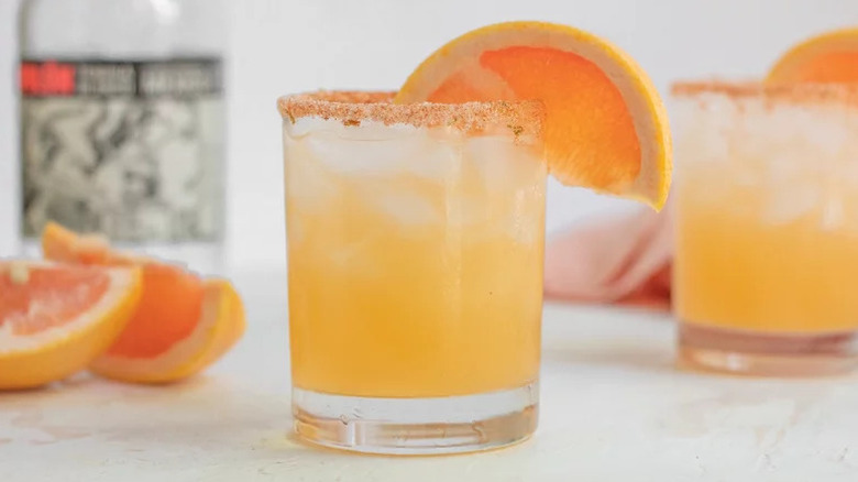 Paloma cocktail in glass with chile salt rim and orange wedge garnish