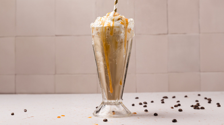 Caramel frappe with coffee beans around against tiled backgroun