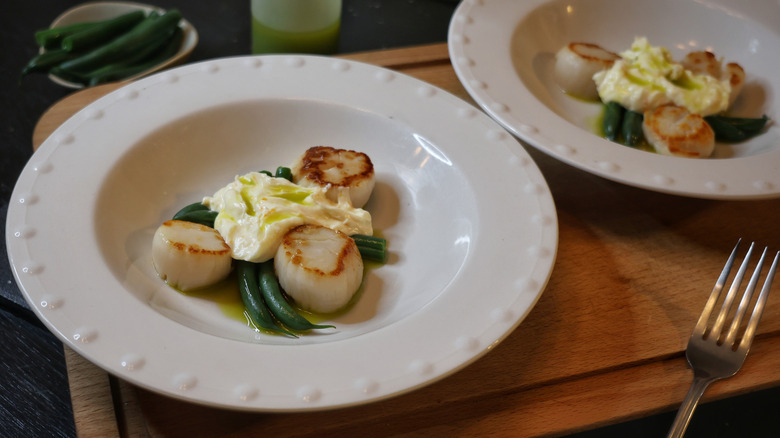 two plates of seared scallops and green beans with orange ginger compound butter and basil oil