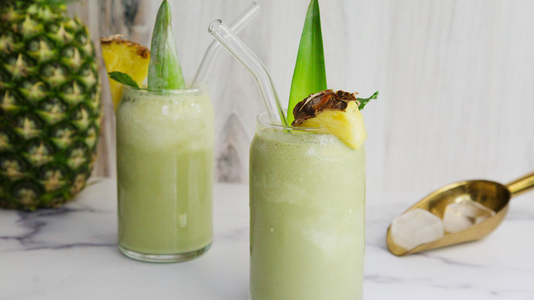 Two green drinks with ice and a pineapple in background
