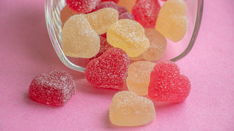 Gummy candy hearts spilling out of a glass onto a pink surface