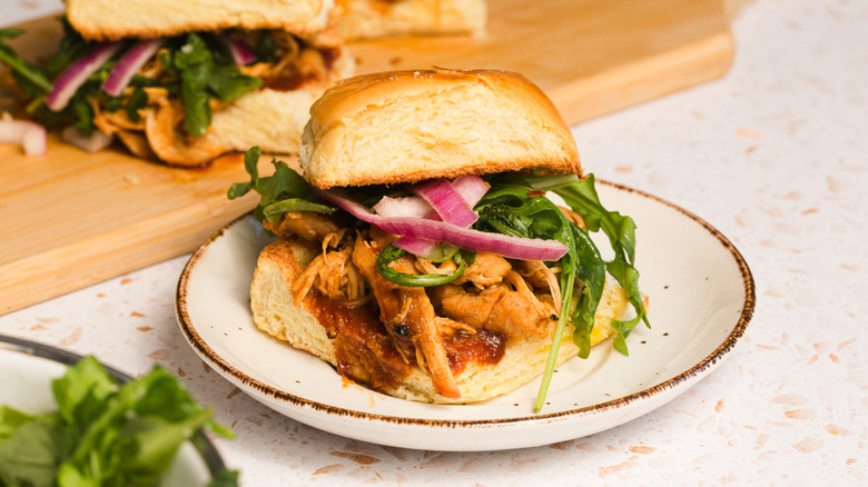 Slider on plate with arugula in front and more sliders on board in background