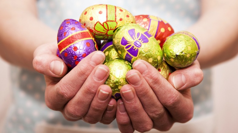Hands holding colorful foil-wrapped chocolate Easter eggs