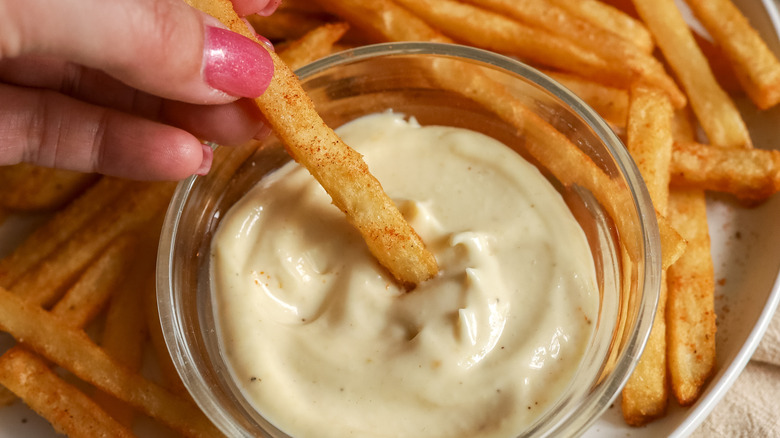 a french fry being dipped in truffle aioli