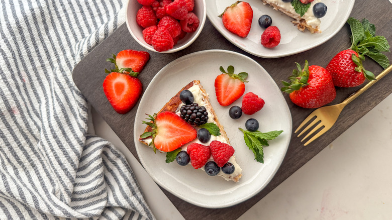 Fruit pizza slice on plate surrounded by strawberries and raspberries