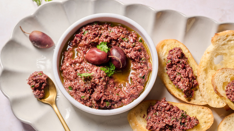 small bowl of tapenade on a serving platter with crostini