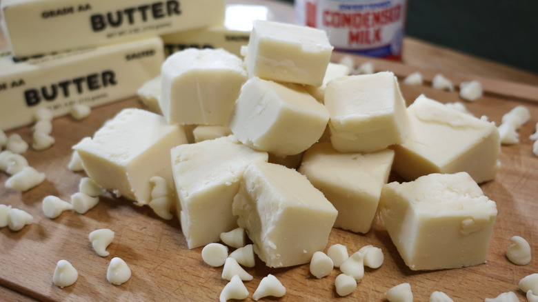 a pile of white chocolate fudge pieces on a cutting board with butter, white chocolate chips, anc condensed milk