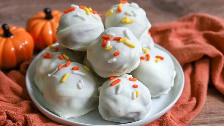 Homemade white chocolate pumpkin truffles on orange kitchen towel with sprinkles