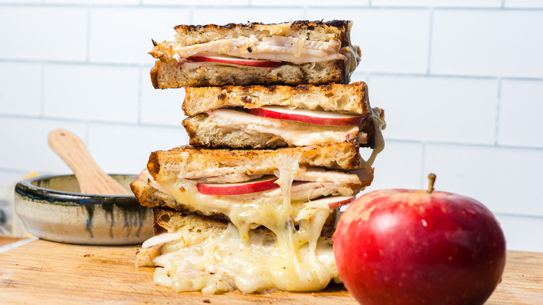 A stack of grilled apple turkey cheddar sandwiches with an apple in front of them