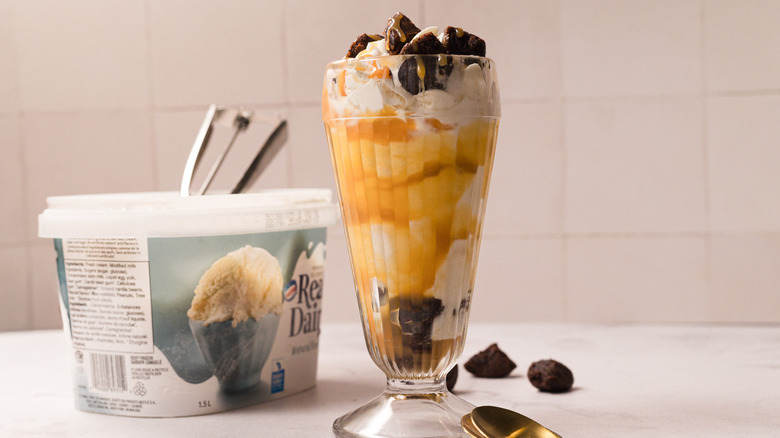 Caramel brownie sundae with large vanilla ice cream pail and a scoop