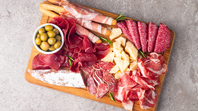 A charcuterie board with various cured meats, bowl of olives, and cubed cheese