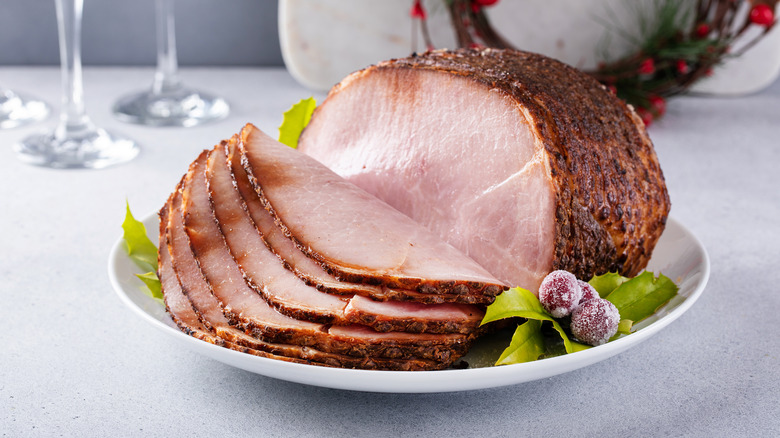 A dark glazed ham set out on a tray with some Christmas garnishes