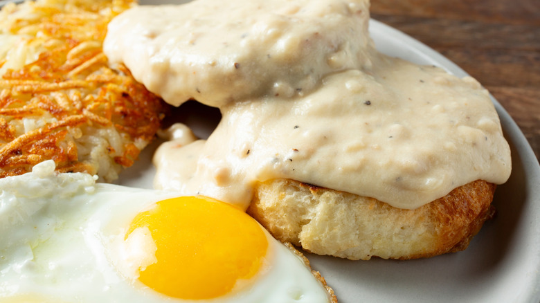 A view of a biscuits and gravy breakfast plate with hash browns and eggs