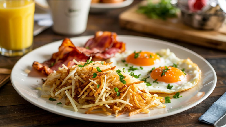 A plate of sunny-side eggs, hashbrowns, and bacon beside a cup of orange juice