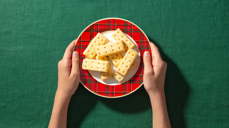 A person holding a festive plate of shortbread cookies on a green tablecloth