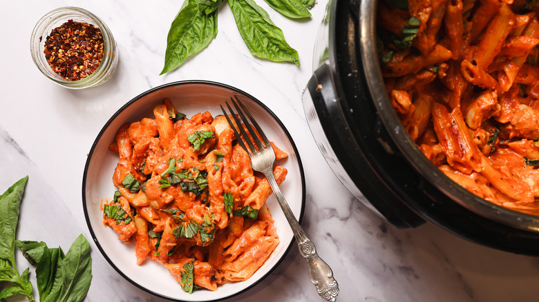 Penne pasta in creamy tomato sauce in bowl with Instant Pot besides it