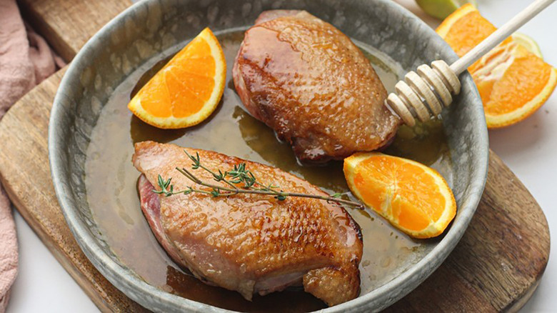 Honey-glazed duck breasts in dish with orange wedges and thyme sprig.