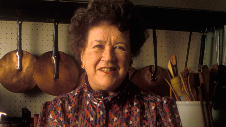 Julia Child stand with her arms folded in her kitchen