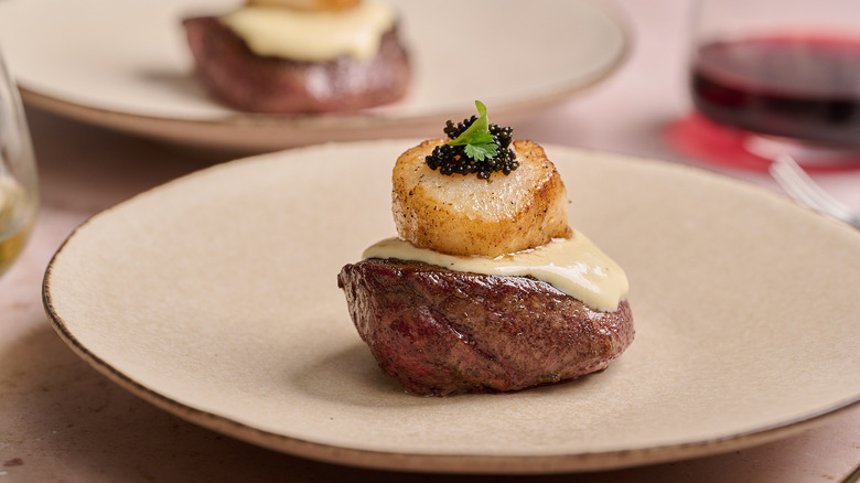 Steak and scallop on a plate with another plate in the background