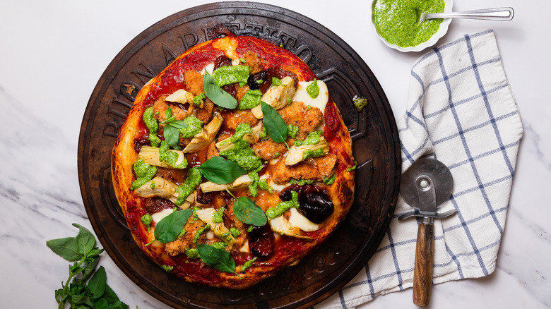 Italian deli style pizza with pizza cutter, napkin, fresh basil and pesto