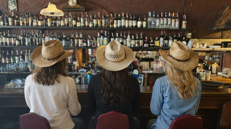 Three people with cowboy hats sitting on stools at My Brother's Bar
