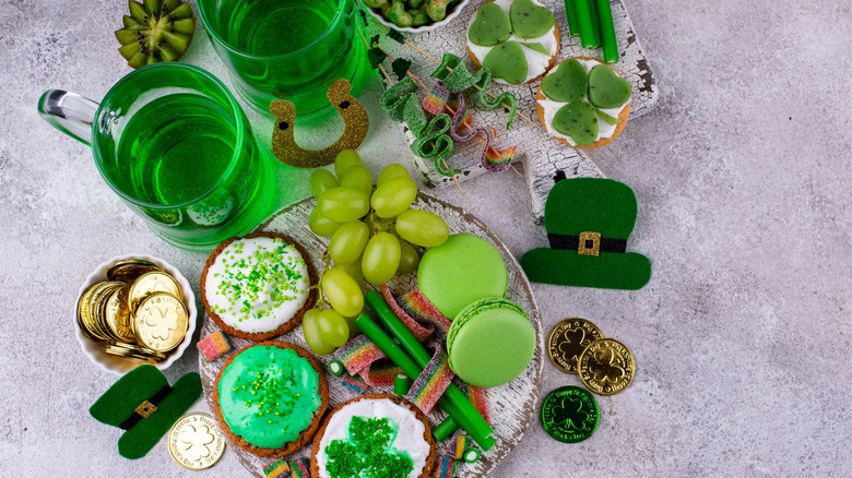 St. Patrick's Day themed foods including green beer, shamrock cookies, chocolate gold coins, green grapes, and green candies