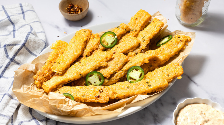 Baked spicy cheese straws on platter beside chili flakes and smoked aioli