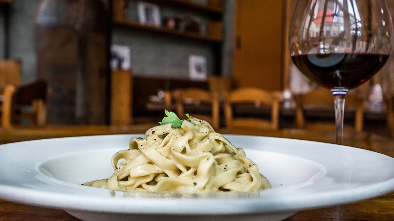 A plate of tagliatelle sits on a table with a glass of red wine next to it.
