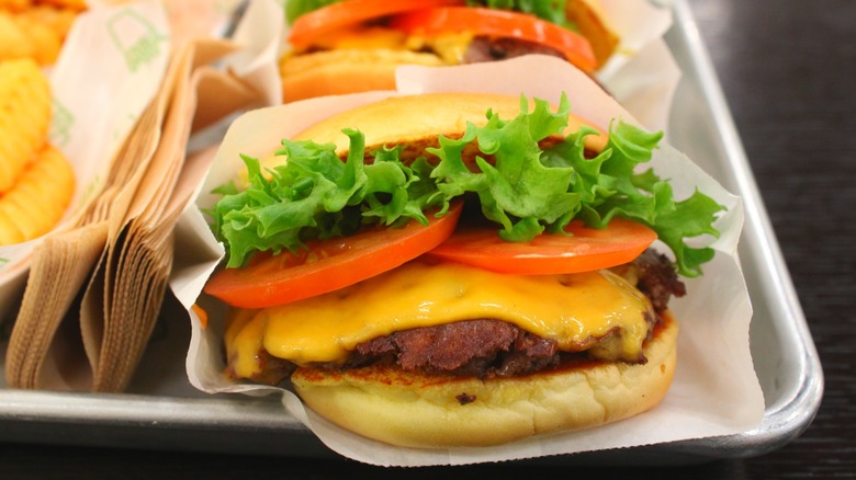 ShackBurger from Shake Shack with lettuce, tomato, and cheese inside paper sleeve on silver tray