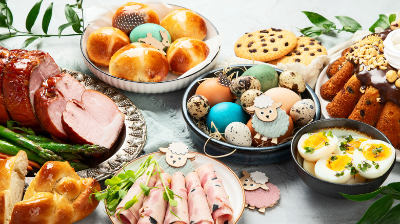 An Easter brunch spread featuring rolls, dyed eggs, and sliced honey-glazed ham with Easter decor