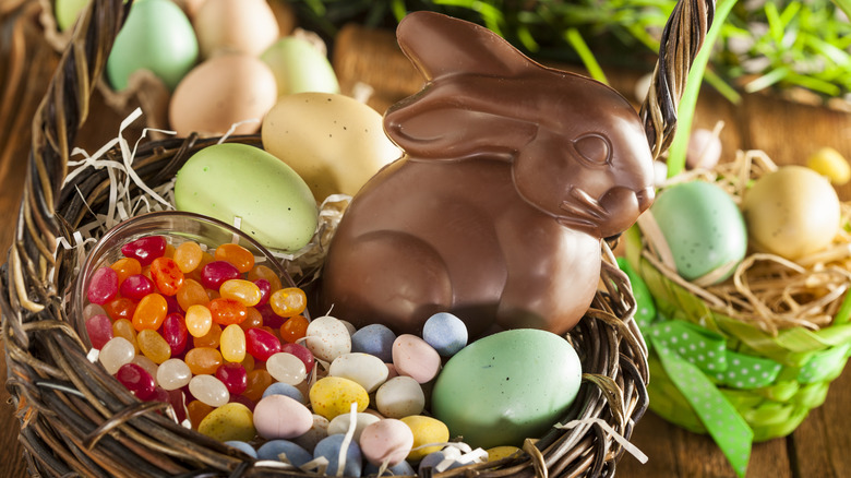Brown woven basket full of Easter items including chocolate rabbit, dyed eggs, chocolate eggs, and jelly beans