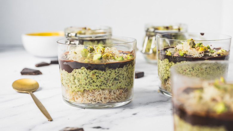 Cups of Dubai style pistachio chia pudding with spoons on a marble countertop.