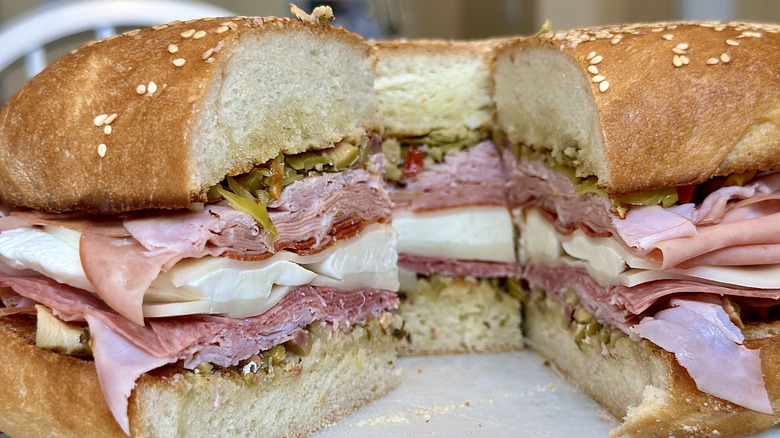 An Italian deli sandwich sliced in thirds and wrapped in deli paper on a white plate