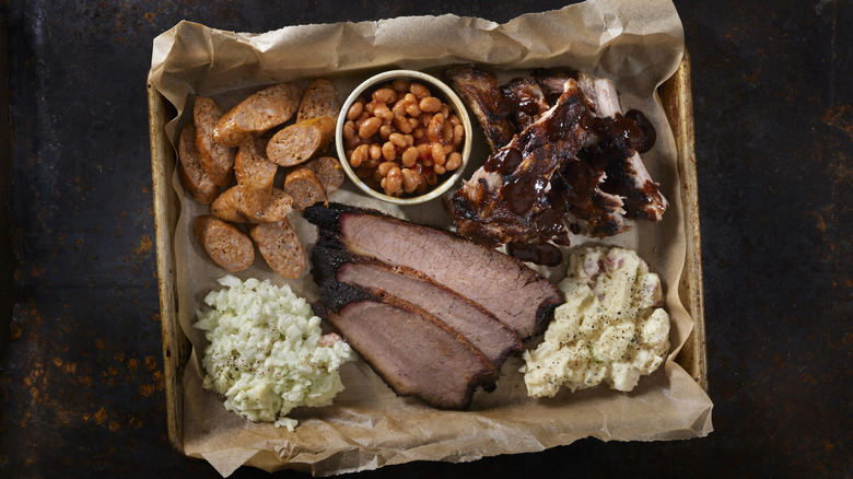 Top view image of a BBQ platter with sausage, brisket, ribs, salads, and beans on brown paper
