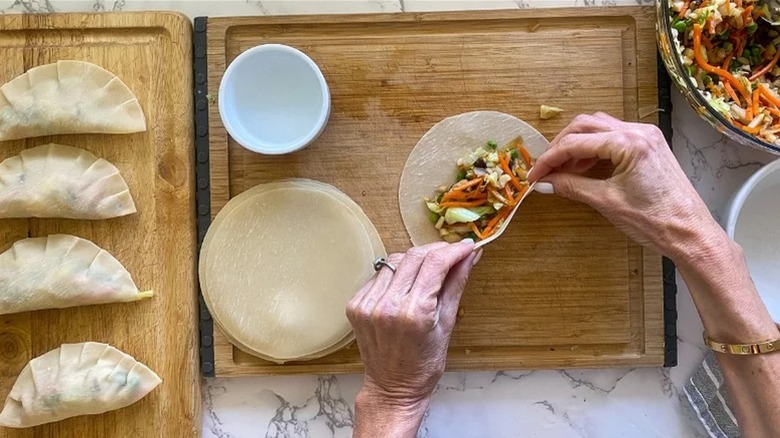 Hands wrapping Homemade Veggie Potstickers on wooden cutting board