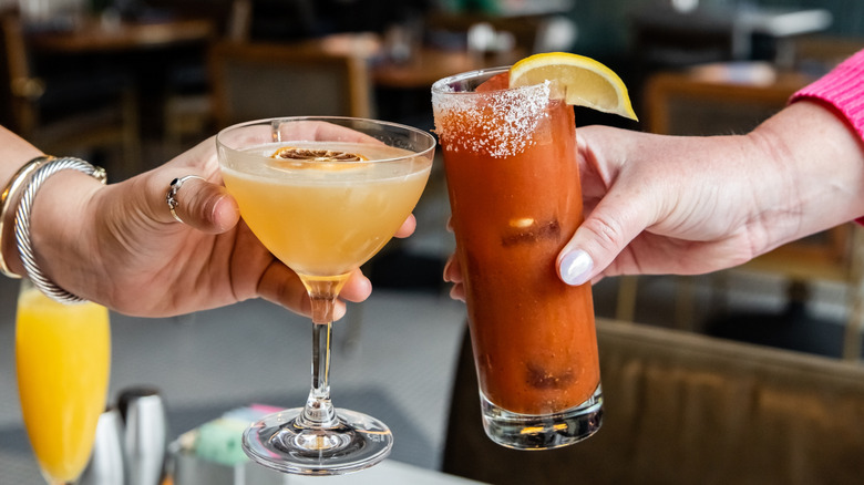 Hands performing cheers with glasses of mimosa and Bloody Mary cocktails inside restaurant