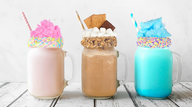 Three summer-themed milkshakes topped with cotton candy and s'mores ingredients