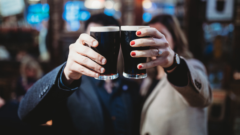 Two people holding up pints of Guinness in a pub with their faces obscured