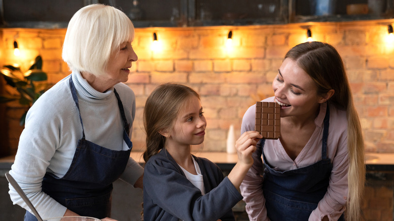 Three generations of women with the youngest daughter feeding her mother a chocolate bar
