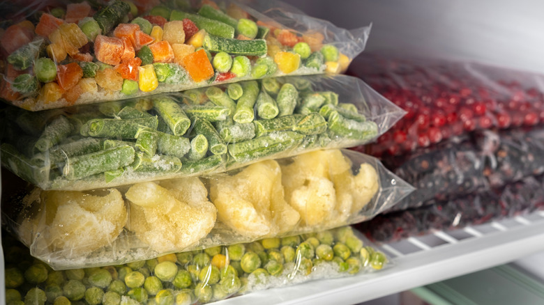 Plastic bags containing peas, cauliflower, green beans, mixed veggies, and berries in freezer