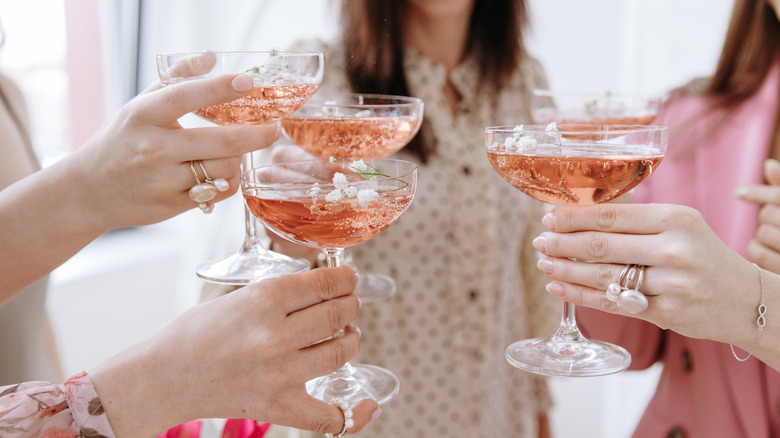 Women toasting holding glasses of rose colored cocktails.