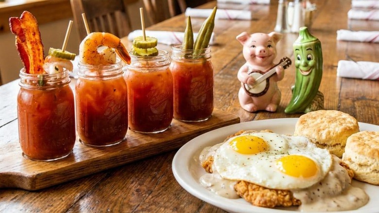 Bloody Mary flight loaded with bacon, shrimp, pickles, and okra sitting next to a plate of biscuits and gravy topped with eggs