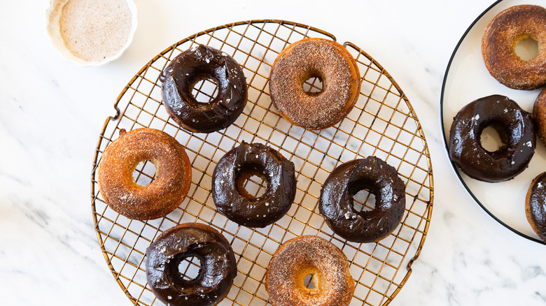 Chocolate and cinnamon sugar baked churro cake donuts on a round drying rack.