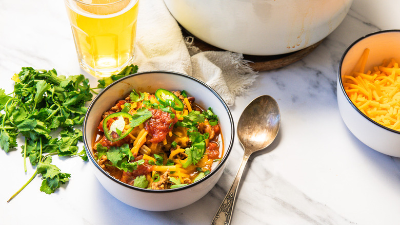 Turkey chili in bowl next to cheese, spoon, and herbs