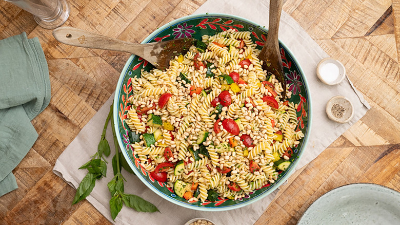 Bowl of fusilli pasta salad with tomatoes, zucchini, and pine nuts