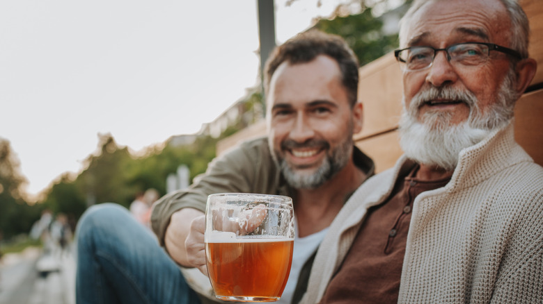 Two men having a beer in mugs outside with one seemingly cheering the camera
