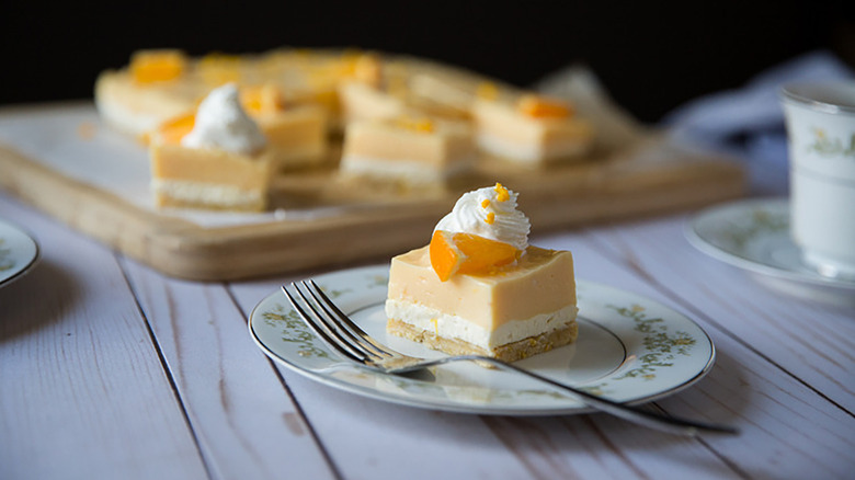 Slice of creamy orange layered dessert on plate, topped with swirl of cool whip and an orange wedge