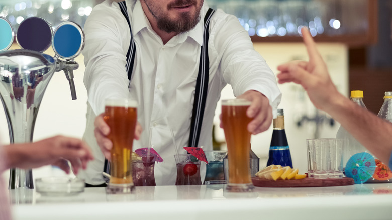 A bartender serves beer to two customers
